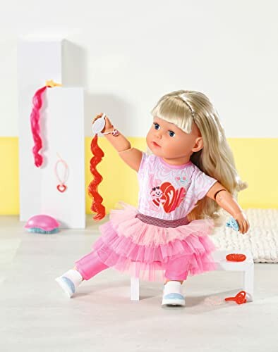 Babypop met blond haar en roze outfit speelt met accessoires.