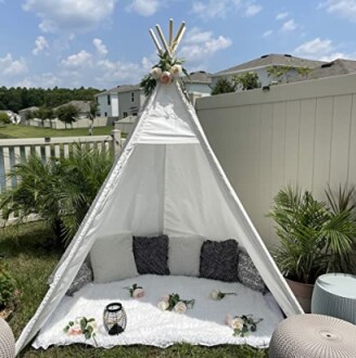 Witte tipi met kussens en bloemen in een tuin.