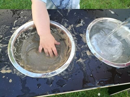 Kind hand speelt met zand en water in metalen kommen.