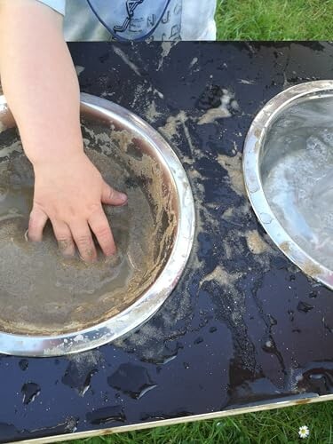 Kind speelt met water en zand in een bak.