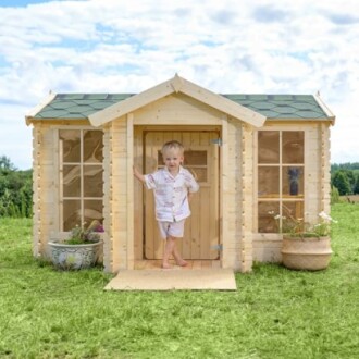 Klein kind bij houten speelhuisje in de tuin.