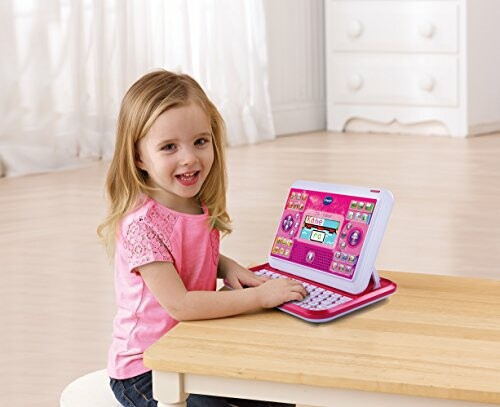 Meisje speelt met roze speelgoedlaptop aan tafel