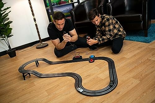 Twee mannen spelen met een speelgoed racebaan op de vloer.