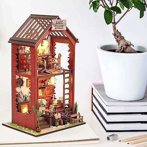 Miniatuur poppenhuis met een plant in een pot ernaast.