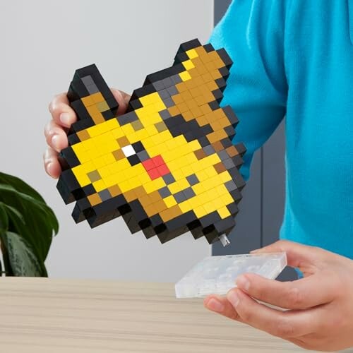 Persoon houdt een pixelachtig geel speelgoedfiguur vast