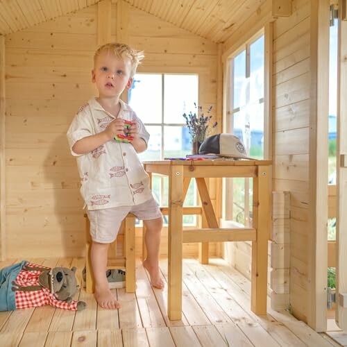 Peuter speelt in houten speelhuis met speelgoed en knuffeldieren.