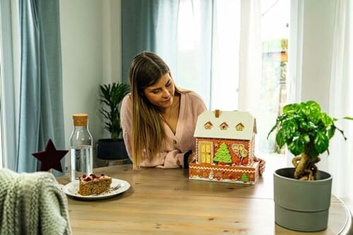 Vrouw kijkt naar peperkoekhuisje op tafel.