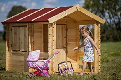 Meisje speelt voor houten speelhuisje met poppenwagen.